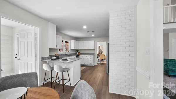 a kitchen with stainless steel appliances kitchen island granite countertop a refrigerator a stove a sink dishwasher and white cabinets with wooden floor