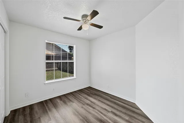 an empty room with wooden floor chandelier fan and windows