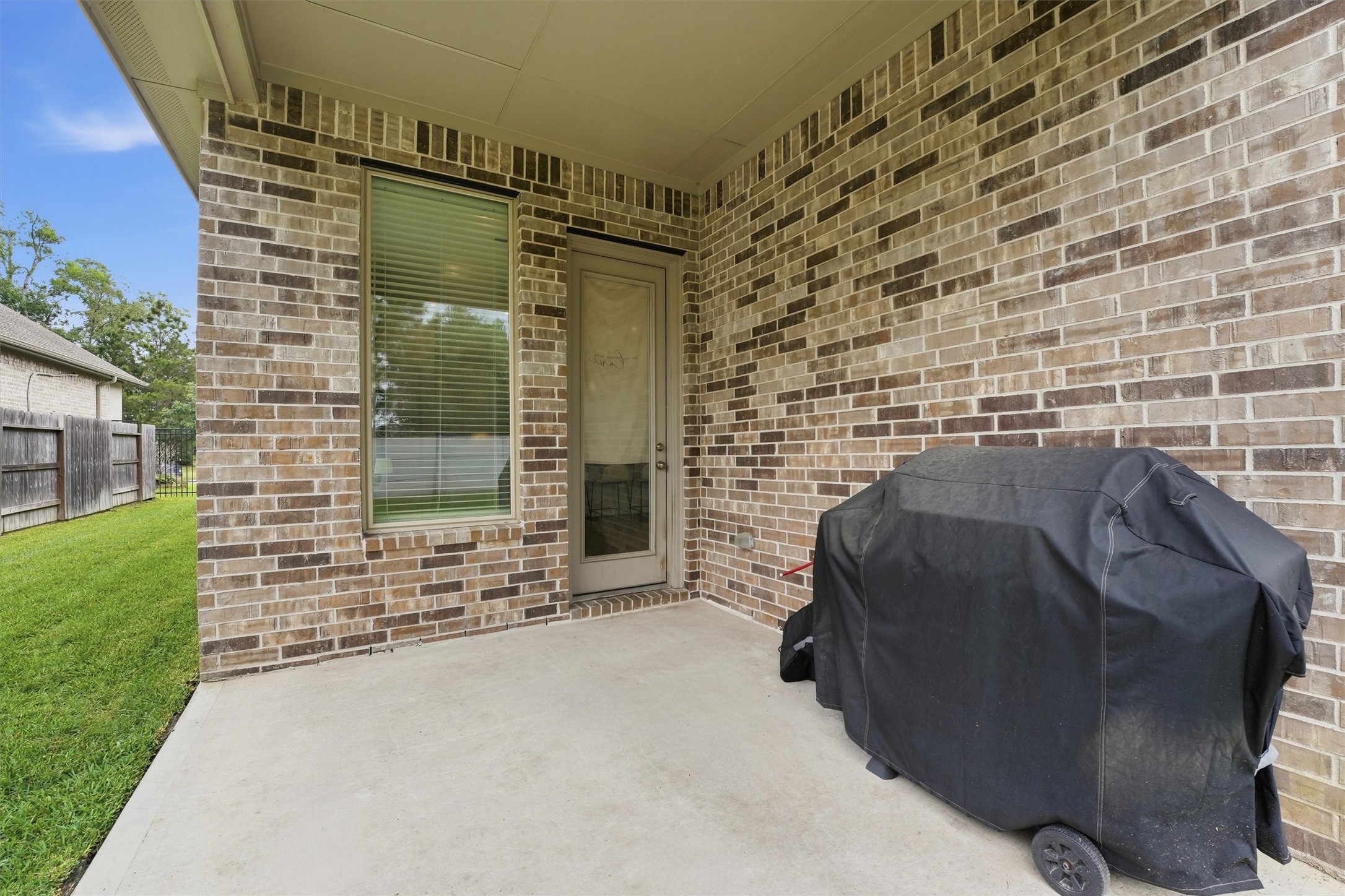6071 Windward Falls Way Porter, TX 77365 - Photo 24 of 33 This photo shows a cozy covered patio with a brick exterior, featuring a door and window, adjacent to a well-maintained lawn.
