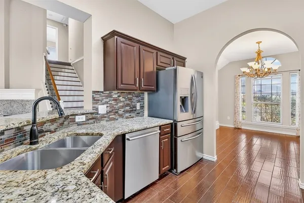 a kitchen with stainless steel appliances granite countertop a sink dishwasher a refrigerator and wooden floor