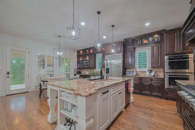 a kitchen with stainless steel appliances granite countertop a stove a sink dishwasher a refrigerator and a kitchen island with wooden floor