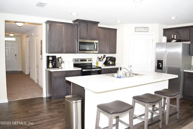 a kitchen with stainless steel appliances a stove a sink a refrigerator and chairs