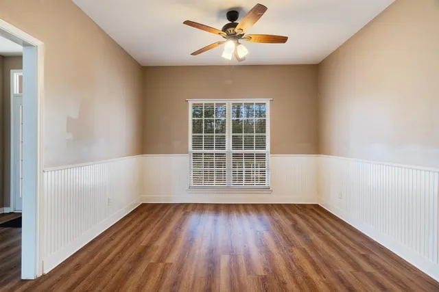 an empty room with wooden floor chandelier fan and windows