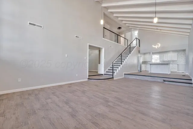 a view of an empty room with wooden floor and stairs