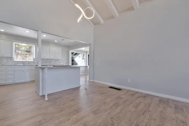 an empty room with wooden floor cabinet and windows