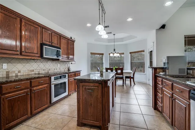 a kitchen with stainless steel appliances granite countertop wooden cabinets a stove top oven a granite counter tops and a view of living room