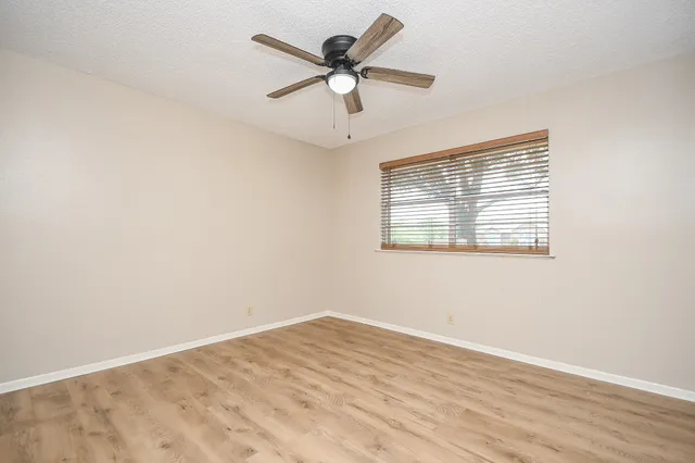 an empty room with wooden floor ceiling fan and windows