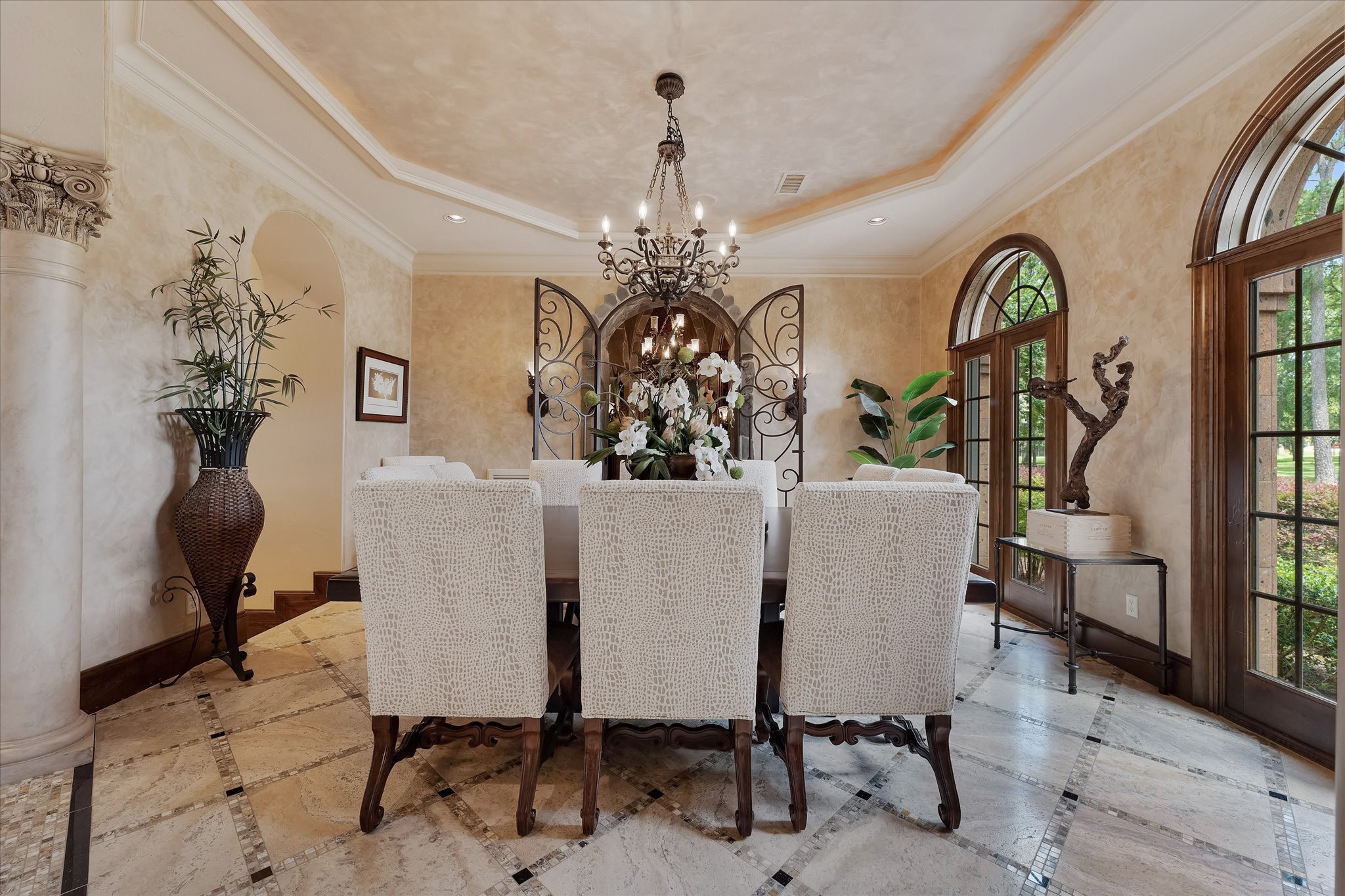 28322 Meadow Forest Magnolia, TX 77355 - Photo 9 of 50 The formal dining room boosts arched columns and travertine flooring with a custom tile pattern. Arched windows overlook the front lawn. Integrate crown molding, recessed speakers, recessed lighting, and a custom chandelier enhance the elegance. The custom tray ceiling with cove lighting and Venetian plastered walls add to the sophisticated ambiance. Custom arched iron gates lead to the wine room, and an arched opening leads to the butler's pantry hallway, providing two different ways to access the kitchen.