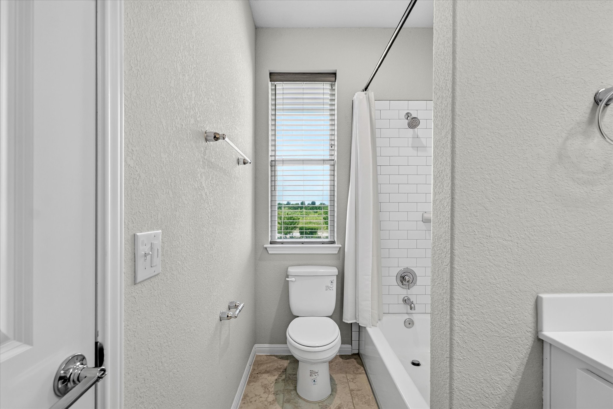 9015 Cattle Baron Path, Unit 1102 Austin, TX 78747 - Photo 19 of 25 A well-lit bathroom features a white subway tile shower, a modern toilet, and an inviting window offering a verdant view.