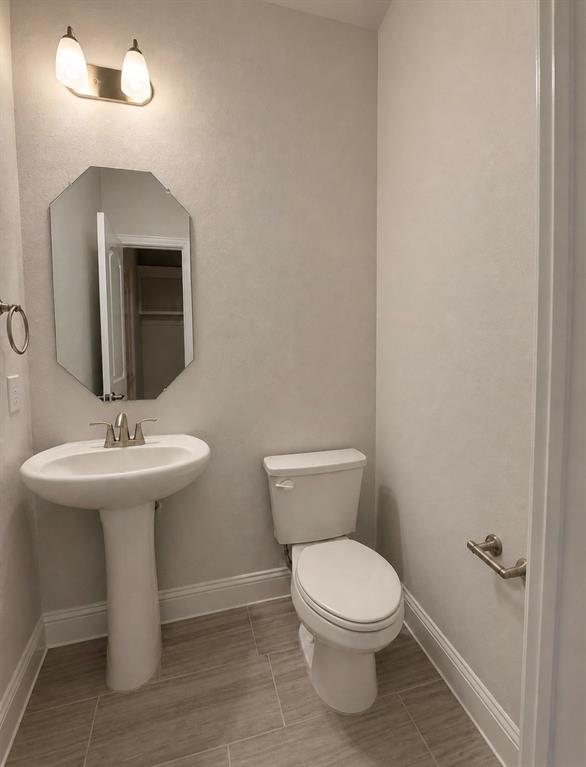 7849 Sunset Boulevard Rowlett, TX 75088 - Photo 5 of 13 Compact bathroom featuring a pedestal sink, white toilet, tile flooring, and a decorative octagonal mirror with an overhead vanity light
