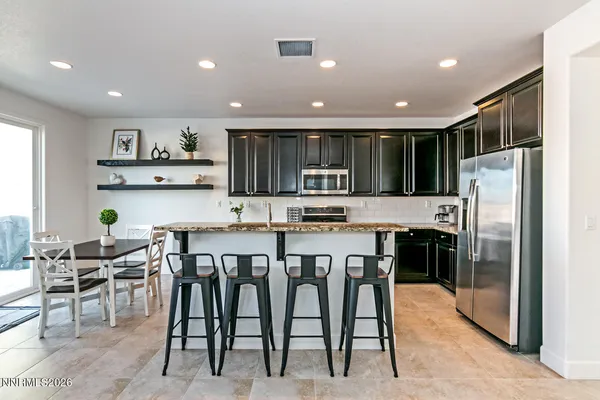 a kitchen with stainless steel appliances granite countertop a refrigerator a stove a sink a dining table and chairs