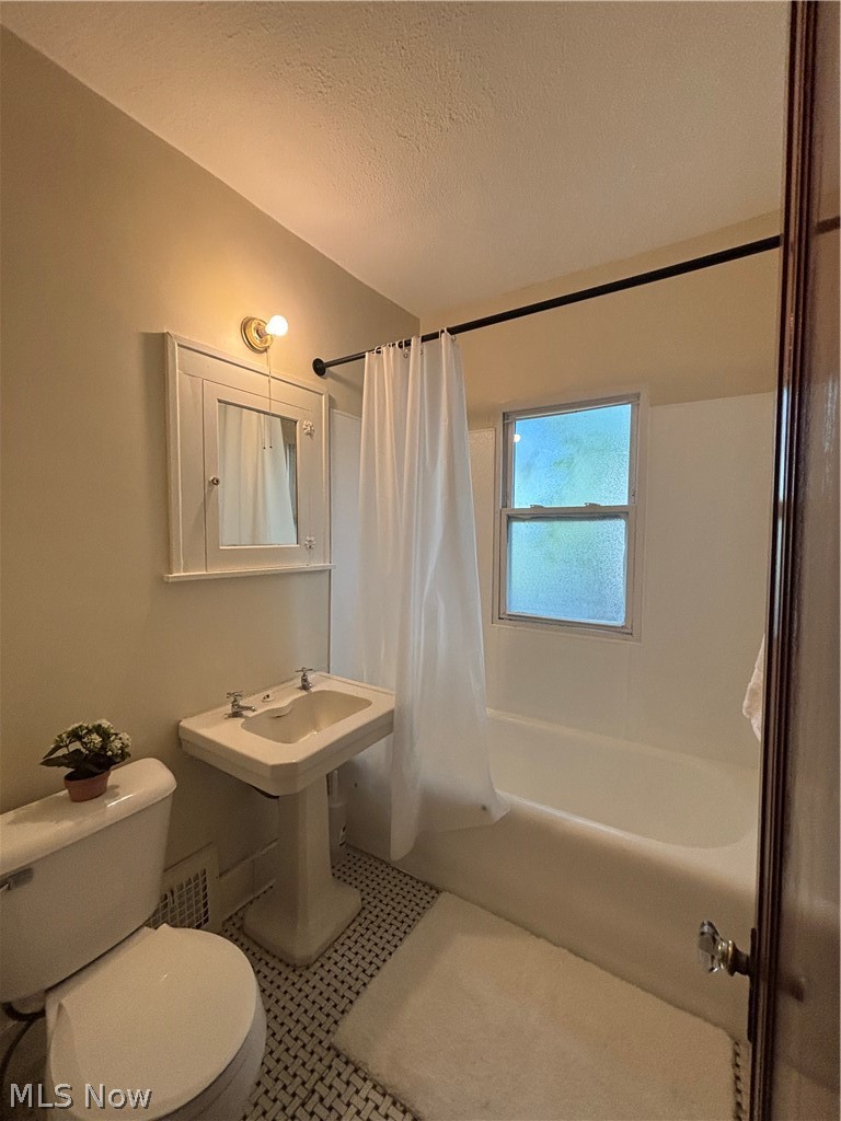 White ceramic pedestal sink and toilet, mosaic tile flooring, built-in medicine cabinet, and a bathtub with a shower curtain rod