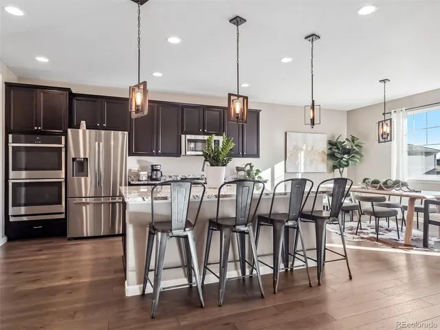 a kitchen with stainless steel appliances kitchen island granite countertop a dining table chairs refrigerator and sink