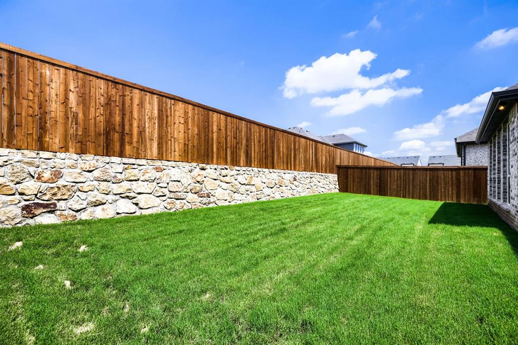 4407 Windy Point Road Oak Point, TX 75068 - Photo 25 of 27 Expansive backyard featuring a manicured lawn, a stone retaining wall, and a full privacy fence