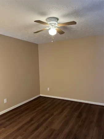 a view of an empty room with wooden floor and a ceiling fan