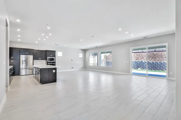 a view of an empty room with kitchen and window