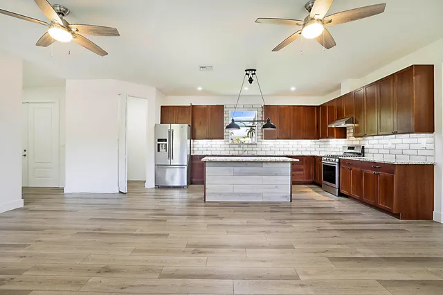 a large kitchen with stainless steel appliances kitchen island granite countertop a stove a refrigerator a sink dishwasher and white cabinets with wooden floor