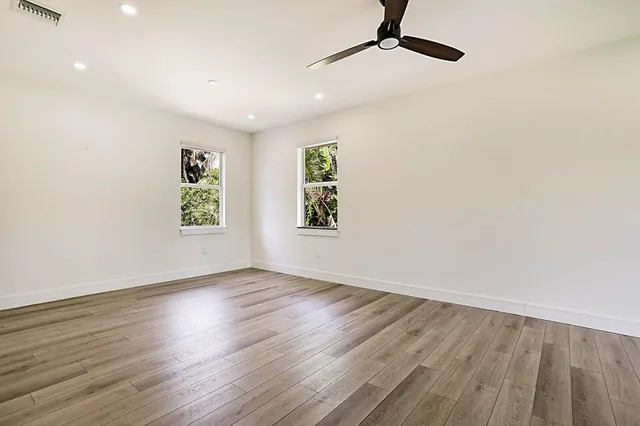 an empty room with wooden floor a ceiling fan and windows