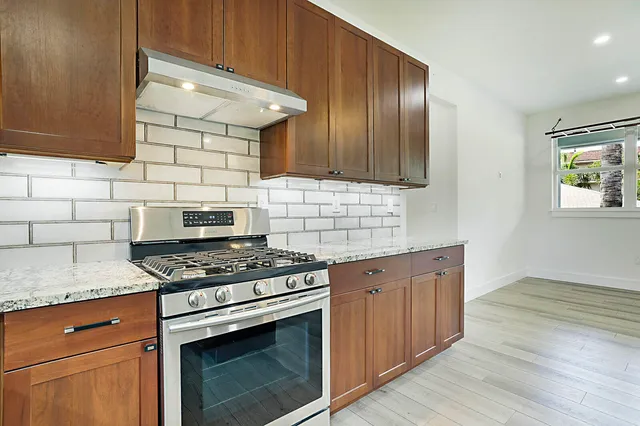 a kitchen with granite countertop stainless steel appliances wooden cabinets and a stove top oven