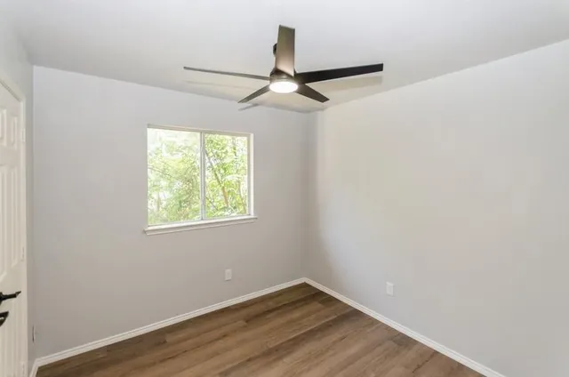 an empty room with wooden floor ceiling fan and windows