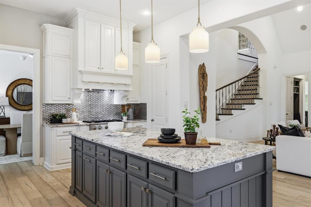 1933 Snapdragon Road Frisco, TX 75033 - Photo 9 of 40 Open-concept kitchen featuring a large island with granite countertops, white cabinetry, a decorative range hood, and a textured metal backsplash