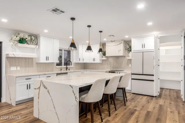 a kitchen with stainless steel appliances kitchen island granite countertop a sink a stove a refrigerator and island with wooden floor