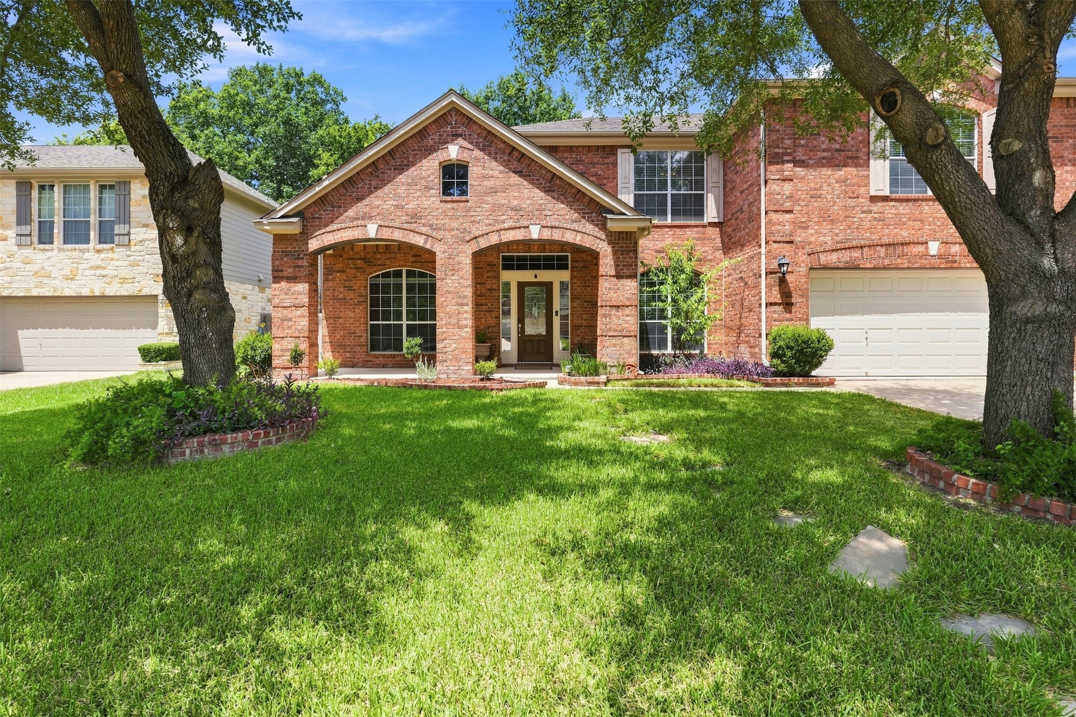 Mature trees shade a classic brick facade with a beautiful arched entryway.