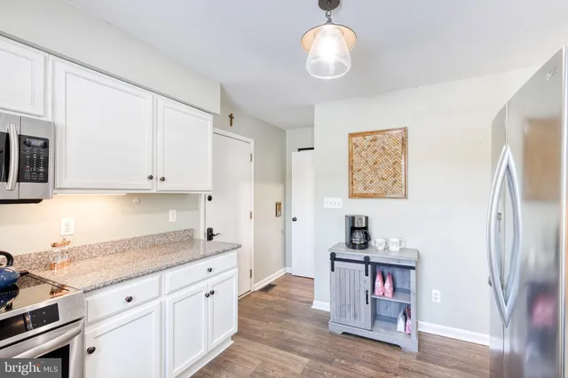 a kitchen with stainless steel appliances granite countertop a refrigerator a stove and white cabinets with wooden floor