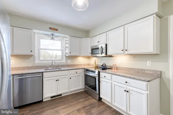 a kitchen with stainless steel appliances granite countertop white cabinets sink and window