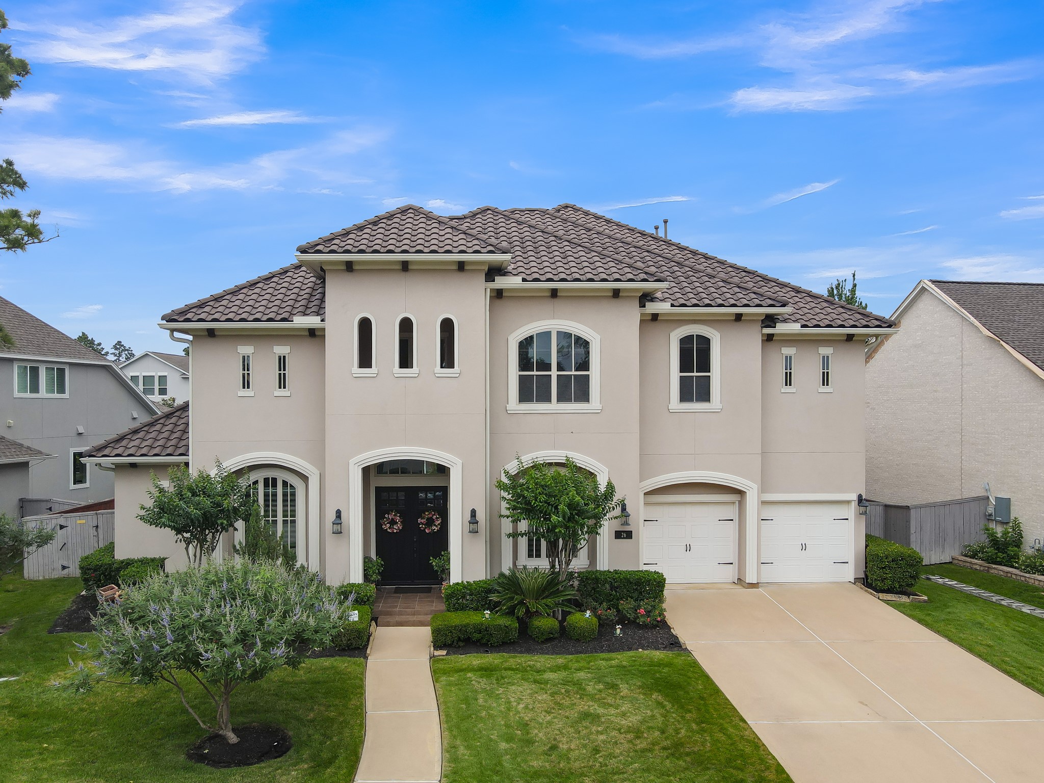 This beautiful two-story home features a stucco exterior with a tiled roof, arched windows, and a three-car garage. The front yard is landscaped with lush greenery and a well-maintained lawn, offering excellent curb appeal.