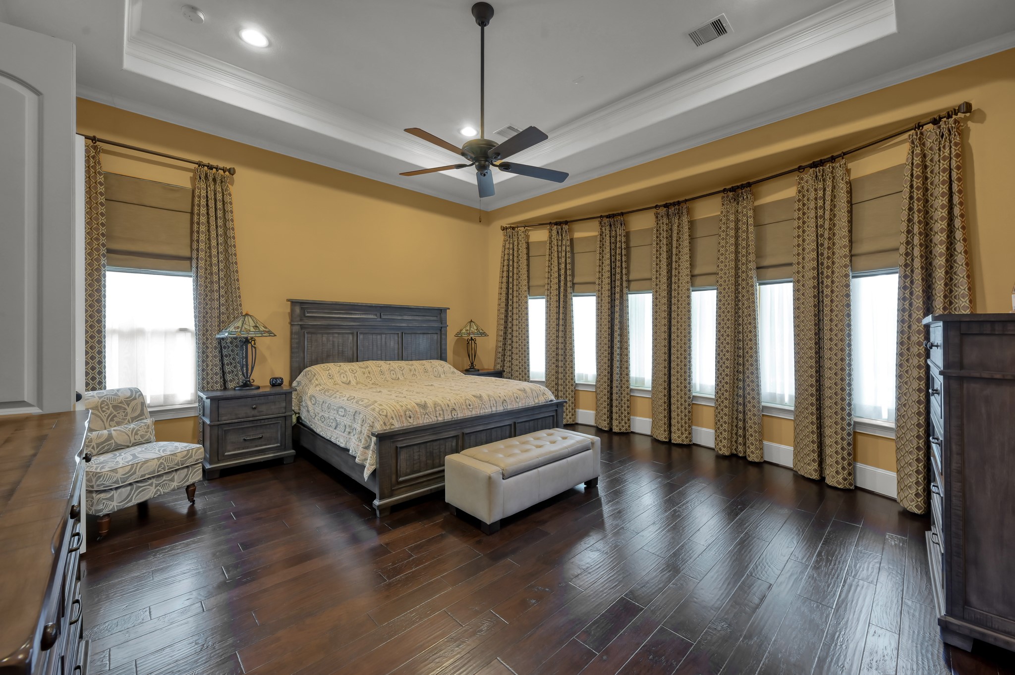 26 Woodborough Way Spring, TX 77389 - Photo 18 of 43 The primary bedroom exudes elegance with its rich wood flooring, warm tones, and abundant natural light filtering through tall windows, creating a serene and inviting retreat.