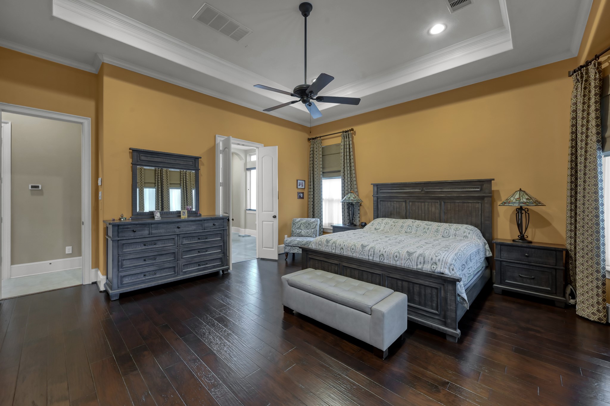 26 Woodborough Way Spring, TX 77389 - Photo 19 of 43 This spacious bedroom features warm yellow walls, dark hardwood flooring, and a tray ceiling with a ceiling fan.