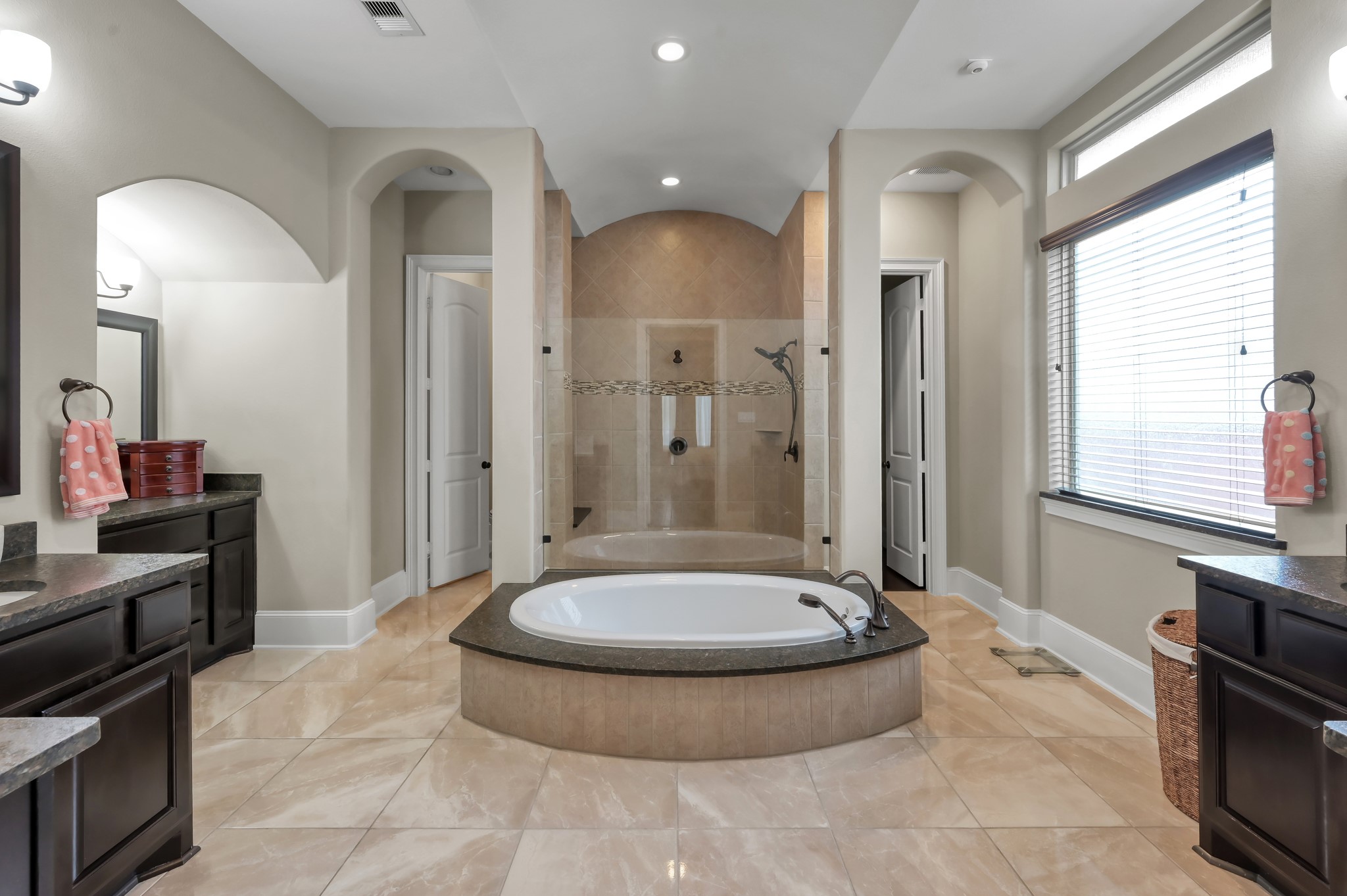 26 Woodborough Way Spring, TX 77389 - Photo 20 of 43 This spacious bathroom features a central soaking tub with dark stone countertops, double vanities, and ample natural light from a large window. It includes a separate walk-in shower and elegant tile flooring, offering a luxurious and functional space.