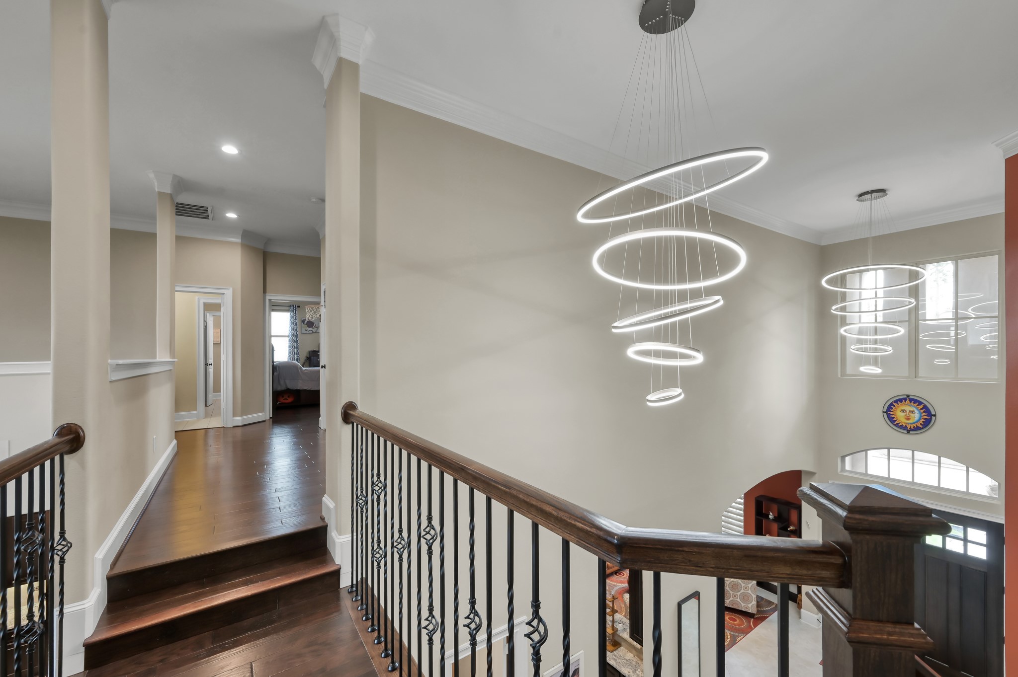 26 Woodborough Way Spring, TX 77389 - Photo 25 of 43 This photo showcases a modern upstairs hallway with elegant wood flooring and stylish railing. The space features contemporary circular pendant lights hanging from the ceiling, adding a touch of sophistication. There are visible entryways to adjacent rooms, offering a glimpse of the home's layout.