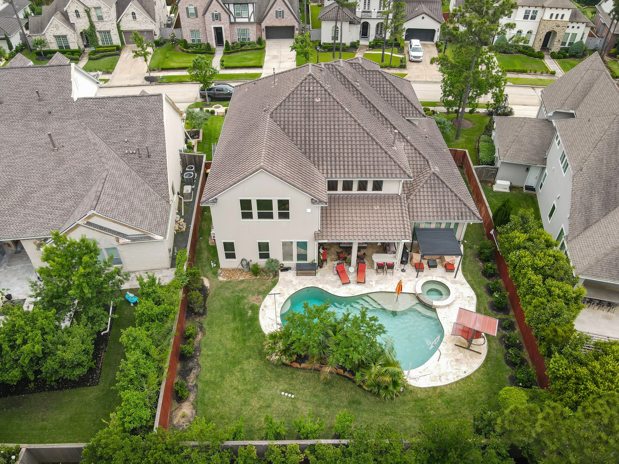 26 Woodborough Way Spring, TX 77389 - Photo 3 of 43 This aerial view showcases a spacious two-story home with a tiled roof, featuring a large backyard with a pool and hot tub. The outdoor space includes a covered patio and is surrounded by well-maintained greenery ideal for relaxation and entertainment.