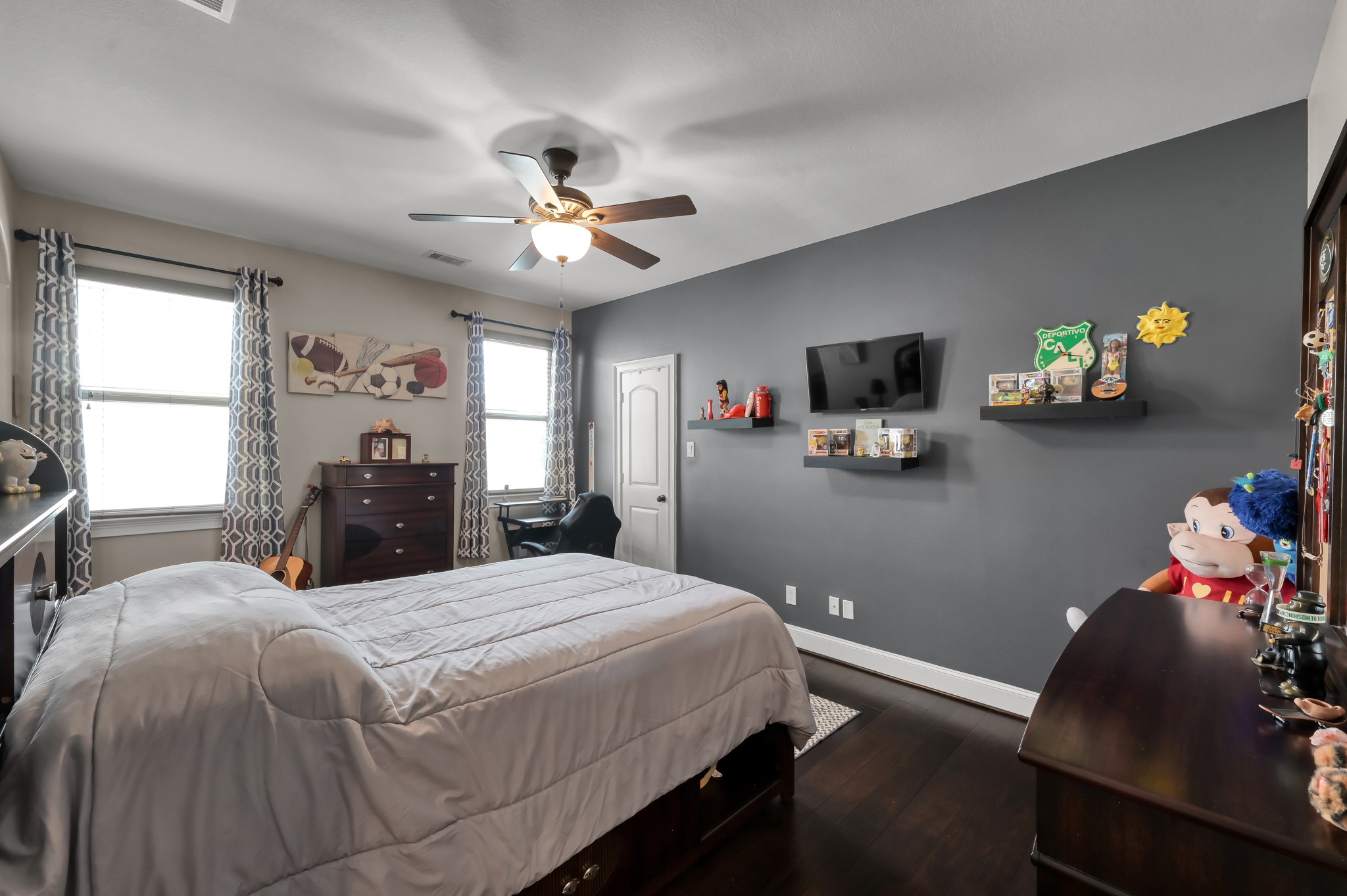 26 Woodborough Way Spring, TX 77389 - Photo 32 of 43 This bedroom features a modern design with dark hardwood flooring and a gray accent wall and two large windows. A ceiling fan and ample natural light enhance the cozy atmosphere.