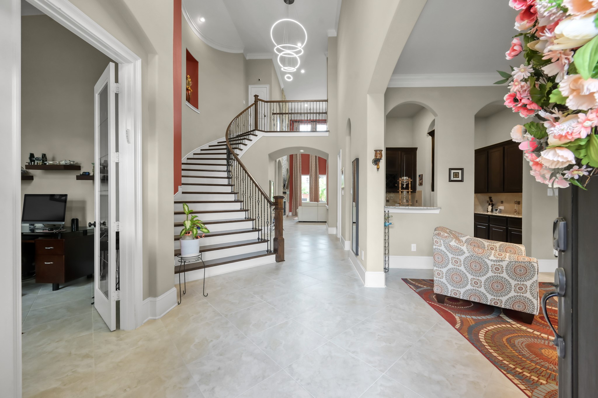 26 Woodborough Way Spring, TX 77389 - Photo 4 of 43 This elegant entryway features a grand curved staircase, high ceilings with modern lighting, and a spacious layout. The area leads to a cozy sitting nook and a home office, with an open view into a stylish kitchen. Perfect for welcoming guests.
