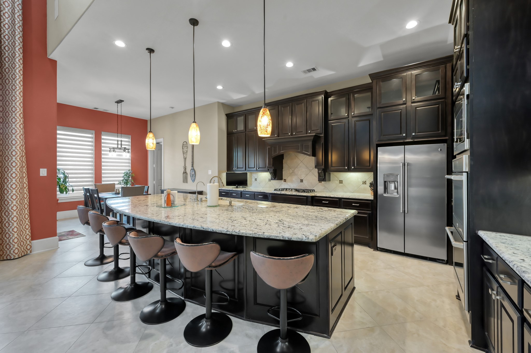 26 Woodborough Way Spring, TX 77389 - Photo 8 of 43 This modern kitchen features a large granite island with plenty of space for seating, stainless steel appliances, and dark wood cabinetry. Ample lighting and an open layout create a welcoming space for cooking and entertaining.