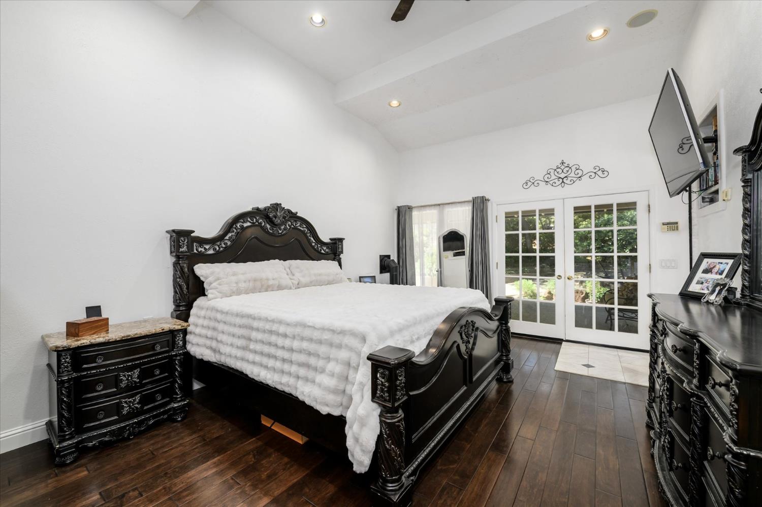 3165 Oakwood Road Cameron Park, CA 95682 - Photo 29 of 55 The romantic primary suite offers it all—soaring vaulted ceilings, a cozy fireplace, and direct outdoor access that fills the space with natural light and fresh air. The spa-inspired ensuite bathroom is finished in marble and tile, creating a refined, luxurious retreat, and features a spacious walk-in closet. Rich wood flooring grounds the room with warmth and timeless elegance.