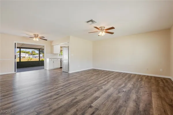 an empty room with wooden floor chandelier fan and windows