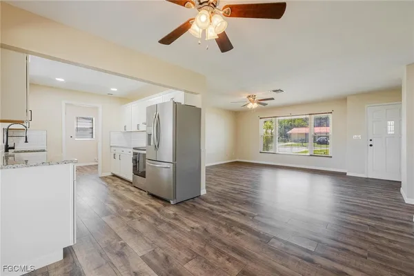 a living room with stainless steel appliances kitchen island granite countertop a refrigerator a stove a microwave oven with white cabinets and wooden floor