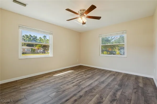 a view of an empty room with wooden floor and a ceiling fan