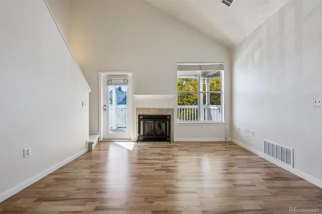 a view of an empty room with wooden floor fireplace and a window