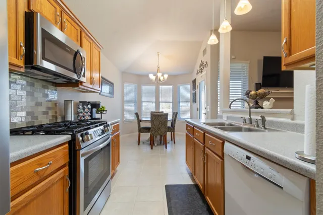 a kitchen with stainless steel appliances granite countertop a stove top oven a sink dishwasher a dining table and chairs with wooden floor