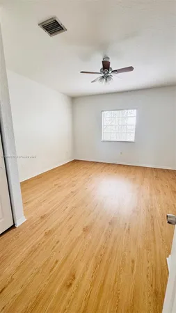 an empty room with wooden floor chandelier fan and windows