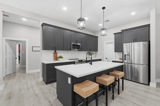 a kitchen with stainless steel appliances a stove a refrigerator a sink a dining table and chairs with wooden floor