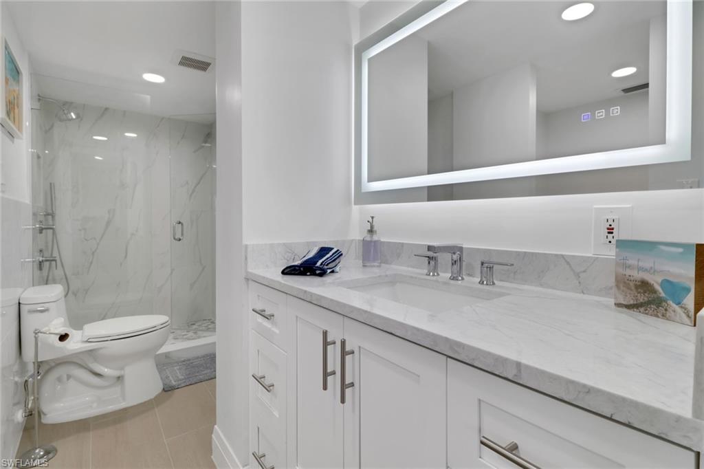 1 Bluebill Avenue, Unit 410 Naples, FL 34108 - Photo 13 of 36 a bathroom with a granite countertop sink mirror vanity and toilet