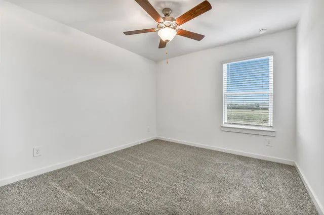 an empty room with chandelier fan and windows