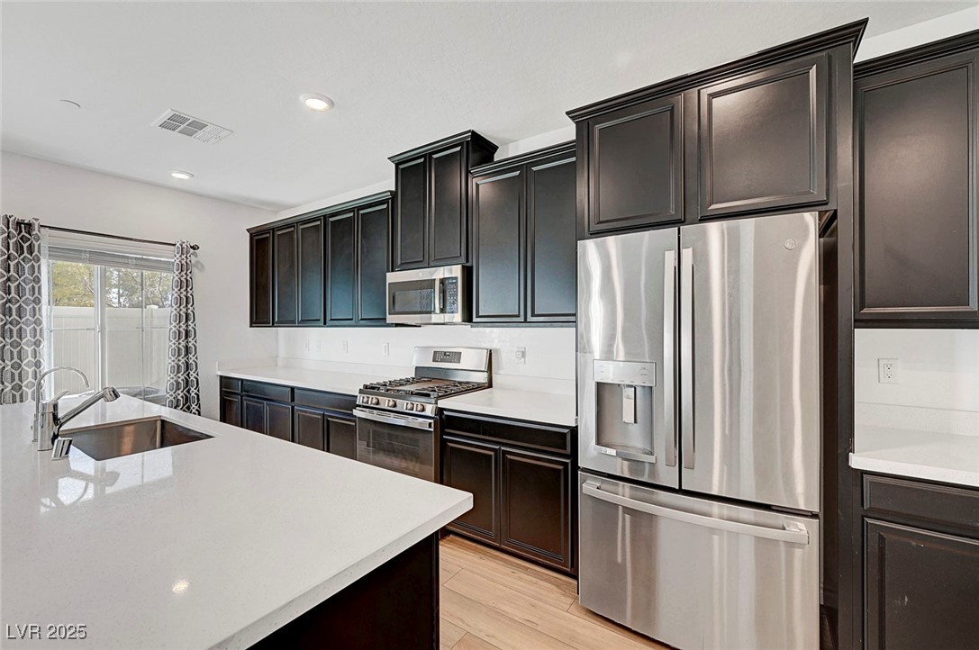 7204 North Decatur Boulevard North Las Vegas, NV 89084 - Photo 21 of 55 Kitchen featuring light countertops, stainless steel appliances, a sink, light wood finished floors, and visible vents