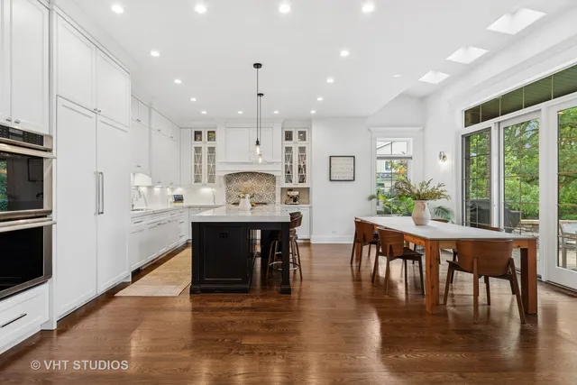 a kitchen with stainless steel appliances granite countertop a stove a refrigerator a kitchen island a dining table and chairs with wooden floor